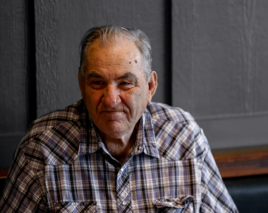 Older man with checkered shirt looking towards camera