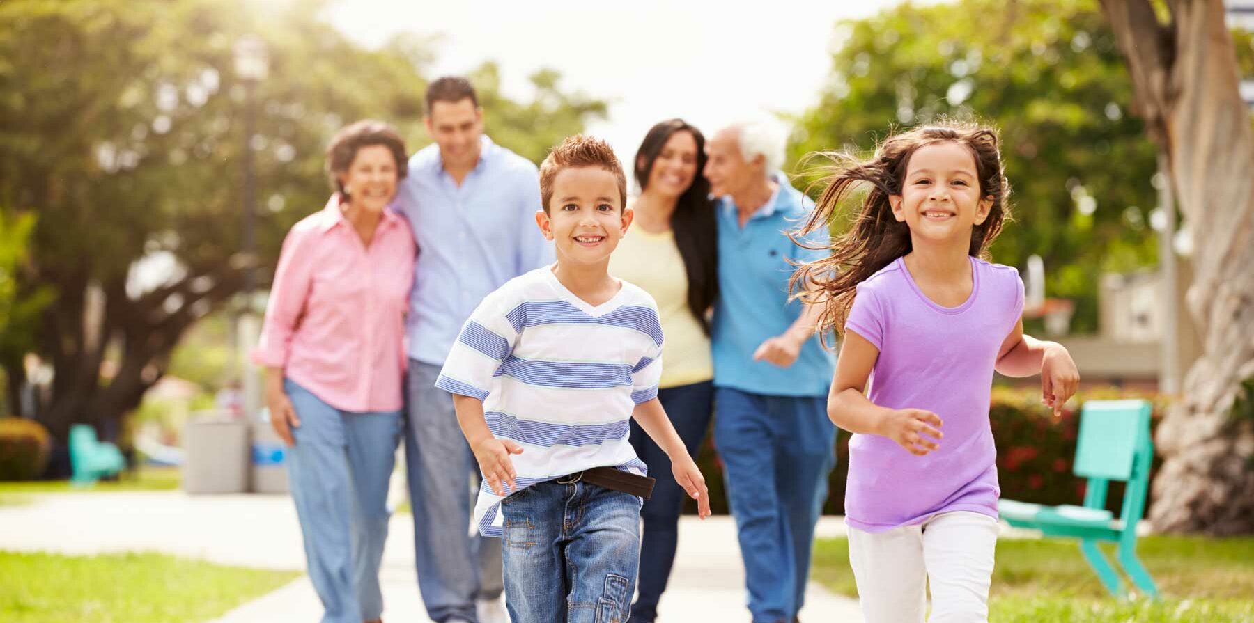 Two kids running toward camera with smiling happy family in background